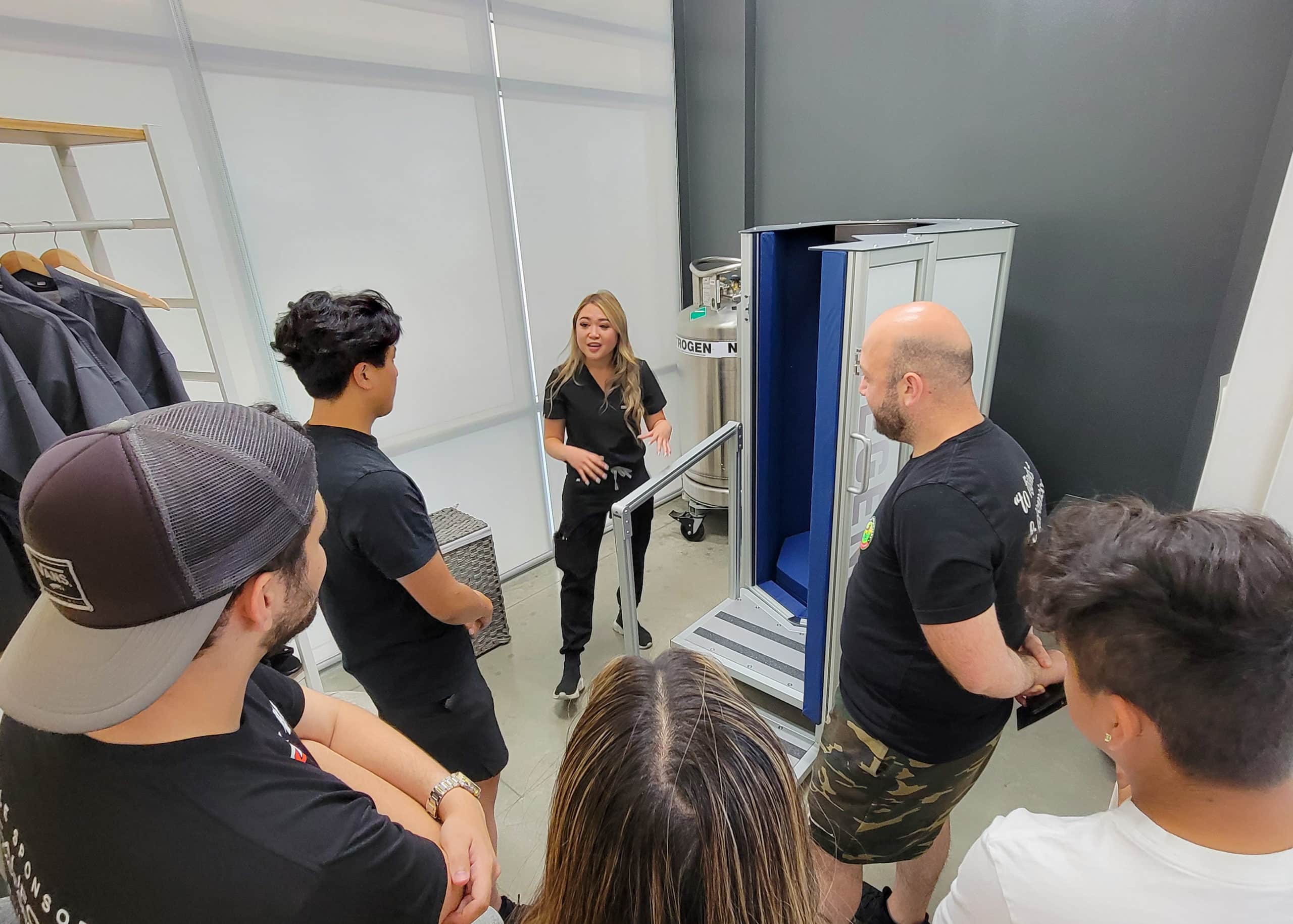 A group of people standing around a machine, discussing the Refer A Friend program.