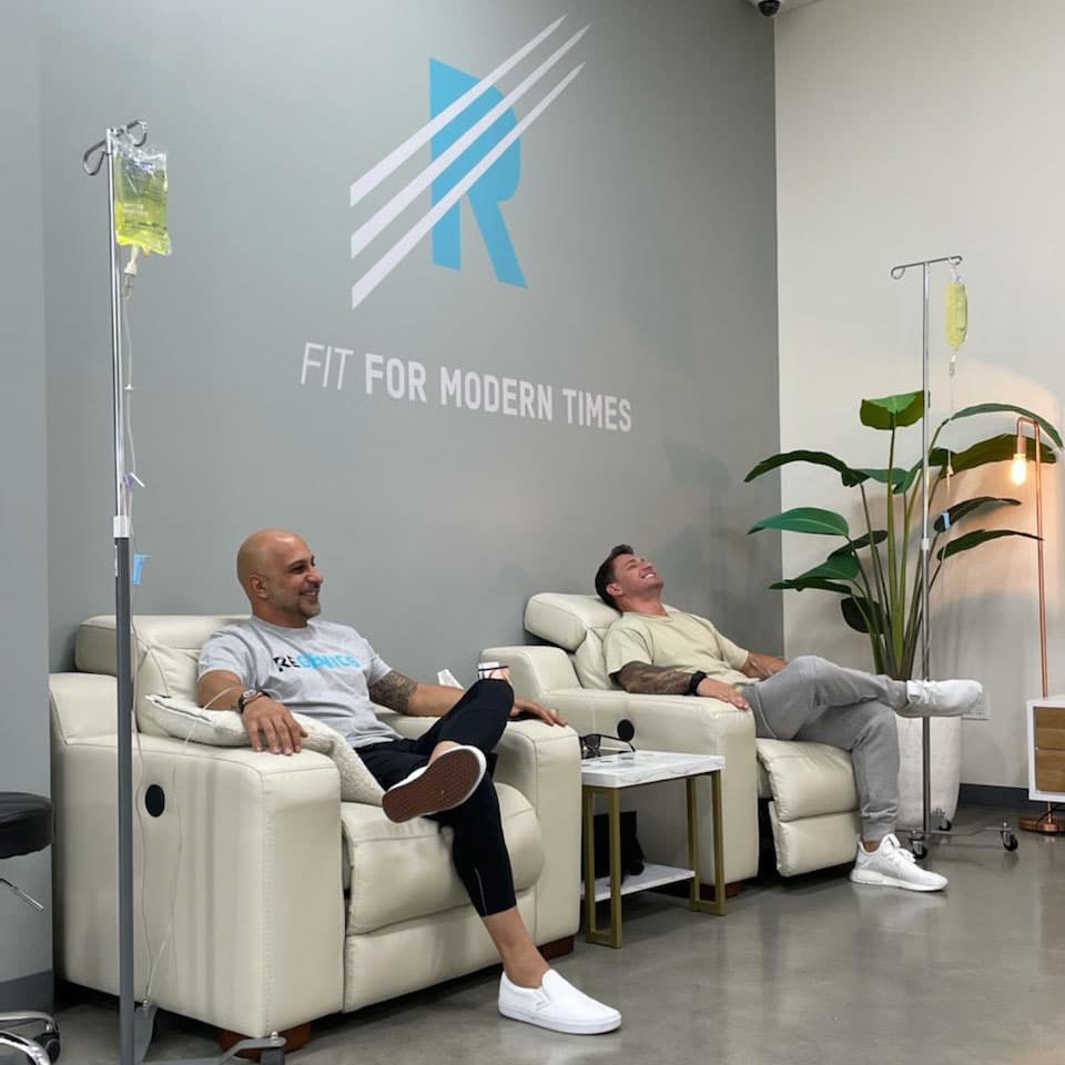 Two men sitting in chairs, undergoing micronutrient testing in a room.