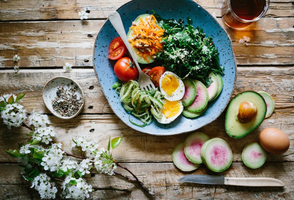 A bowl of salad with eggs and vegetables on a wooden table, perfect for those seeking food sensitivity testing.