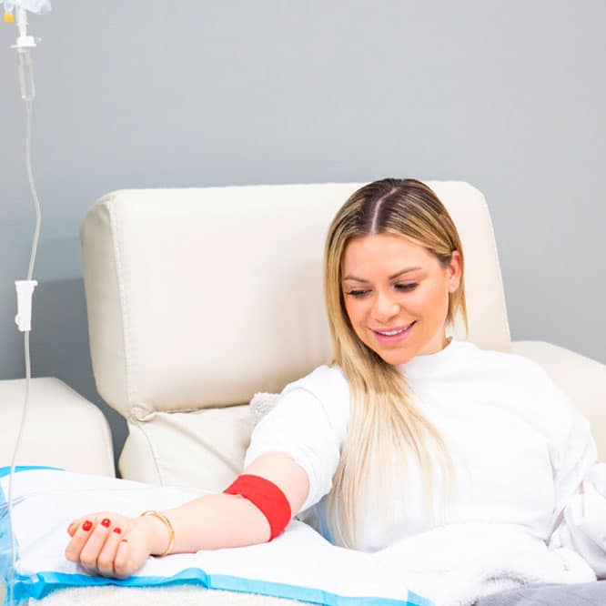 A woman sitting in a hospital bed with a blood iv.