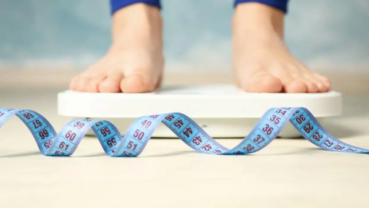 A person's feet standing on a scale with blue tape, showing the weight measurement.