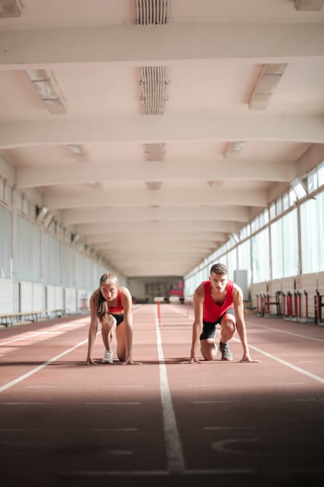 Two people crouching on a running track, training for a sprint with Sermorelin.