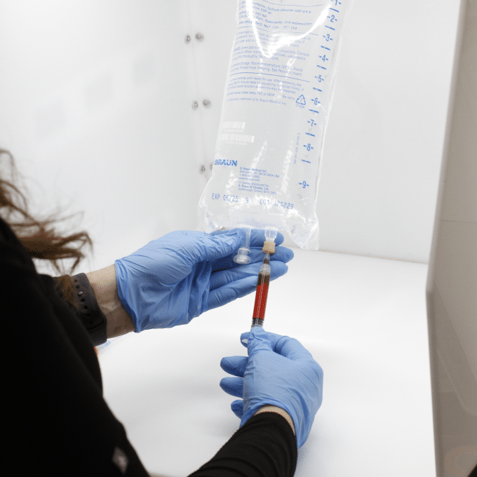 A person in blue gloves holding a bag of blood for IV infusions.