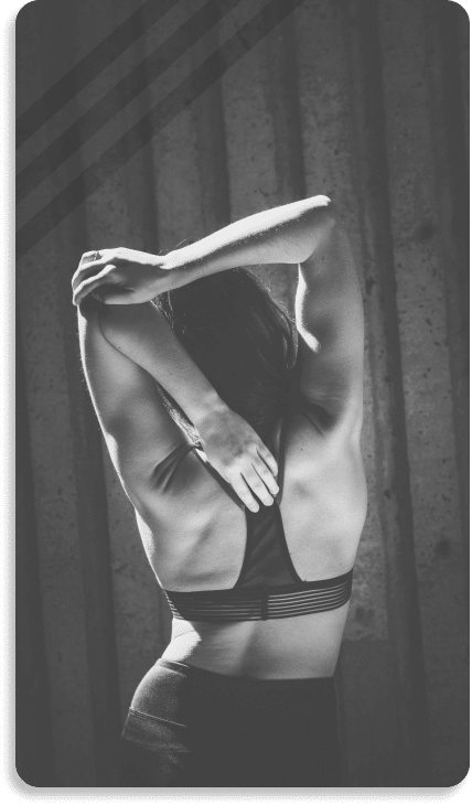 Black and white image of a woman stretching her arms behind her back, wearing a sports bra, against a corrugated metal backdrop, featured in the Header Mega Menu.