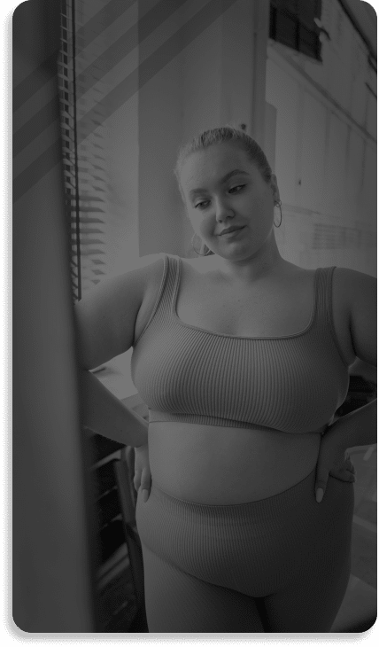 A black and white photo of a woman in a matching activewear set, standing by a window, looking at the camera. This image could be used in the header mega menu of a website design.