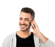 A smiling man with a beard and mustache is holding a cellphone to his ear. He is wearing a black shirt and a light gray hoodie.