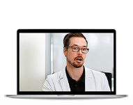 A man wearing glasses and a white coat is displayed on the screen of an open laptop, discussing compounded Tirzepatide treatments.