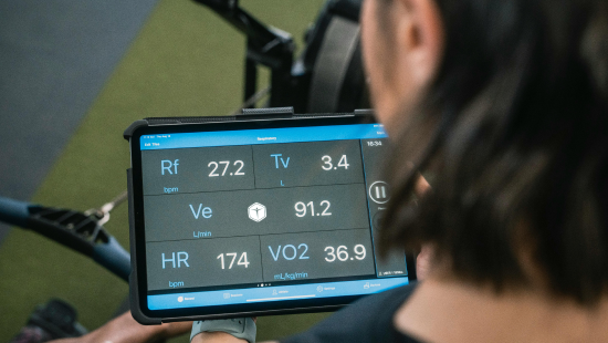 A person holding a tablet in a workout setting showcases fitness metrics, including heart rate and VO2 levels, powered by Regenics Prime technology.