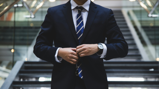 A poised individual in a suit adjusts their jacket on the stairs, showcasing a prime example of sophistication with a striped tie and a Regenics watch.