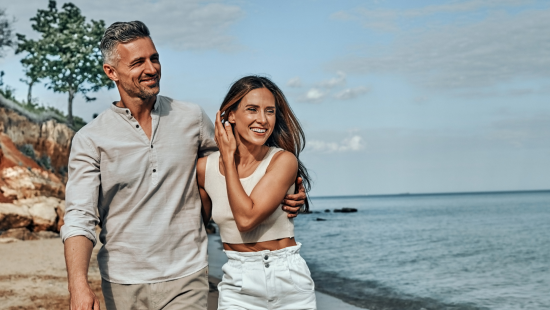 A couple walks along a pristine beach, smiling and enjoying a sunny day. The vast ocean serves as the perfect backdrop to their prime moment together.