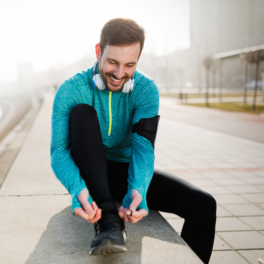 A man in athletic wear, radiating confidence and boosted testosterone levels, ties his shoe while sitting on a concrete bench.