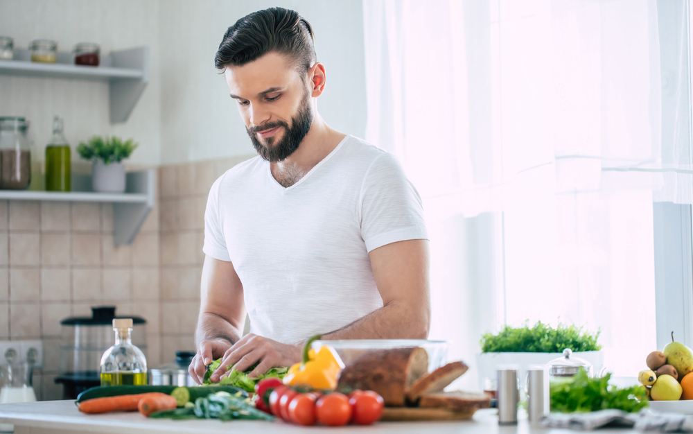 Handsome smiling young bearded man cooks fresh healthy vegan salad