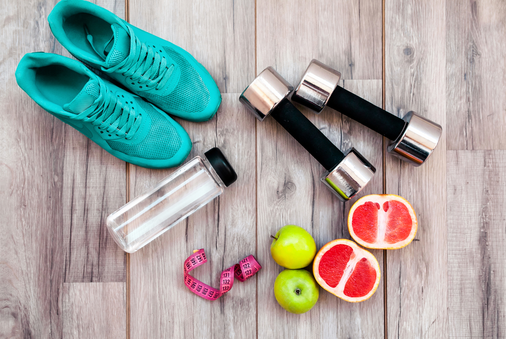 Fitness equipment. Healthy food. Sneakers, water,apple on wooden background.