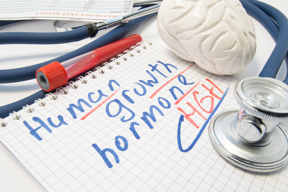 Note inscribed with Human Growth Hormone (HGH) or Somatotropin is surrounded by laboratory test tube with blood, brain figure and stethoscope