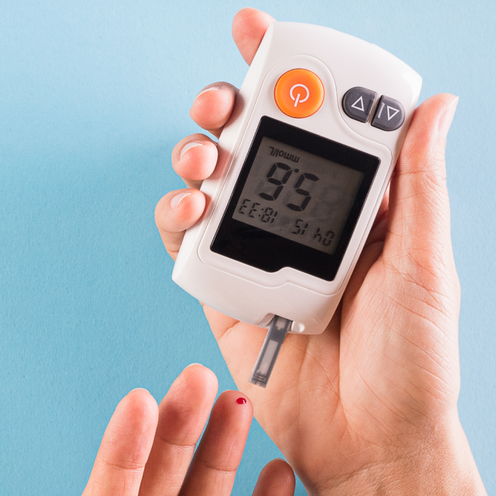 A person holds a glucose meter displaying a reading of 95 mg/dL. A small drop of blood is visible on their fingertip against a blue background.