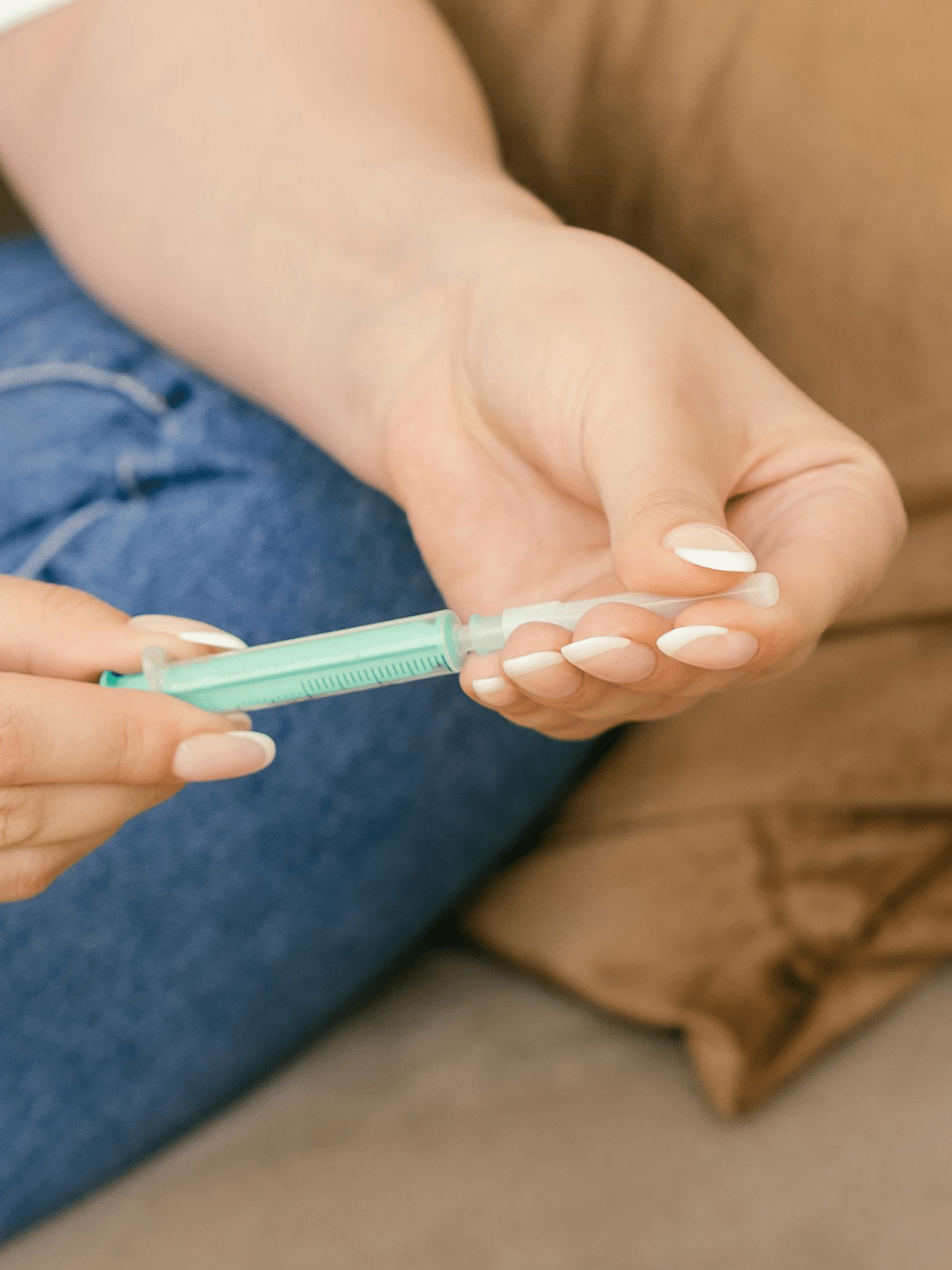 Seated comfortably on a sofa with a brown pillow, a person meticulously examines an Elementor-crafted guide, all while holding a green syringe with a needle cap in one hand.