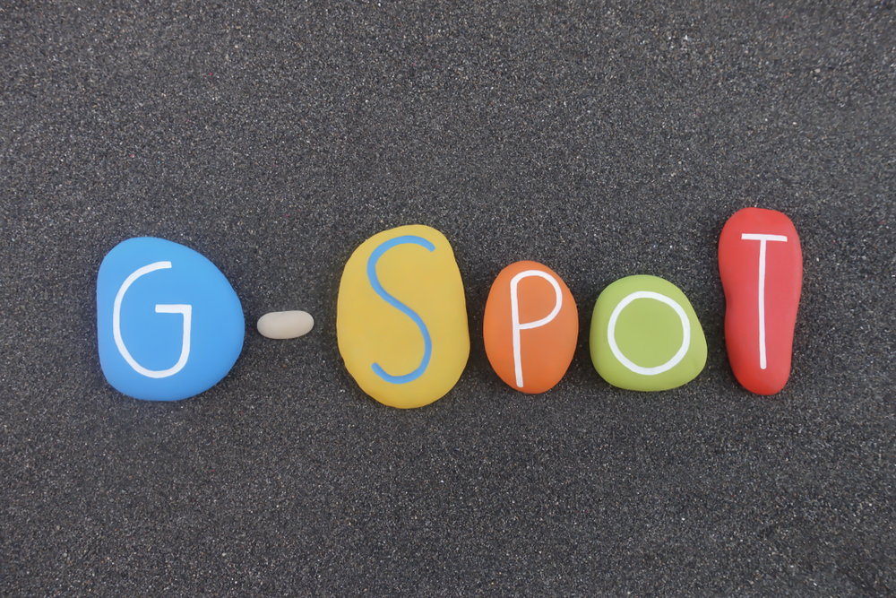 G-Spot erogenous zone emblem text composed with multi colored stones over black volcanic sand