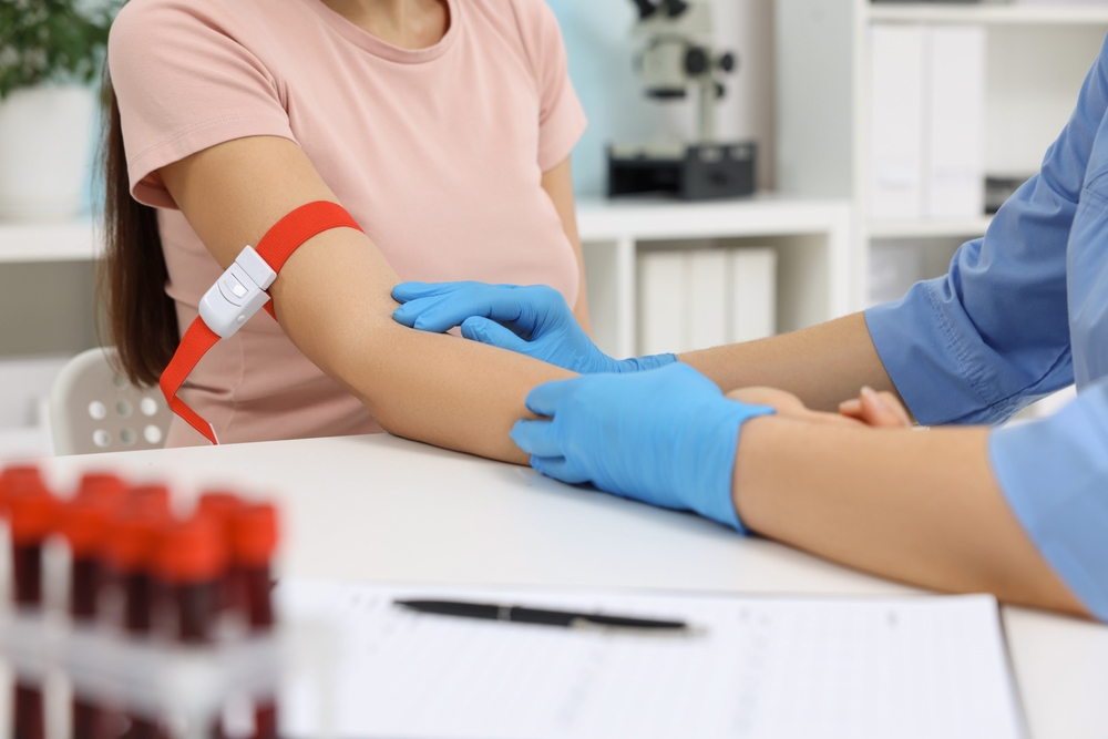 Doctor taking blood sample from patient at white table in hospital