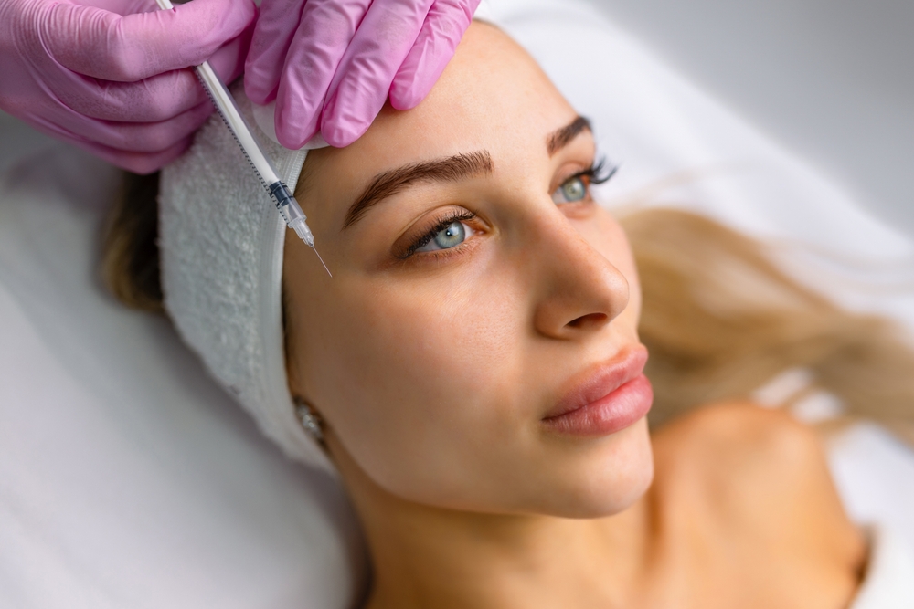 Close up of hands of young cosmetologist injecting botox in female face