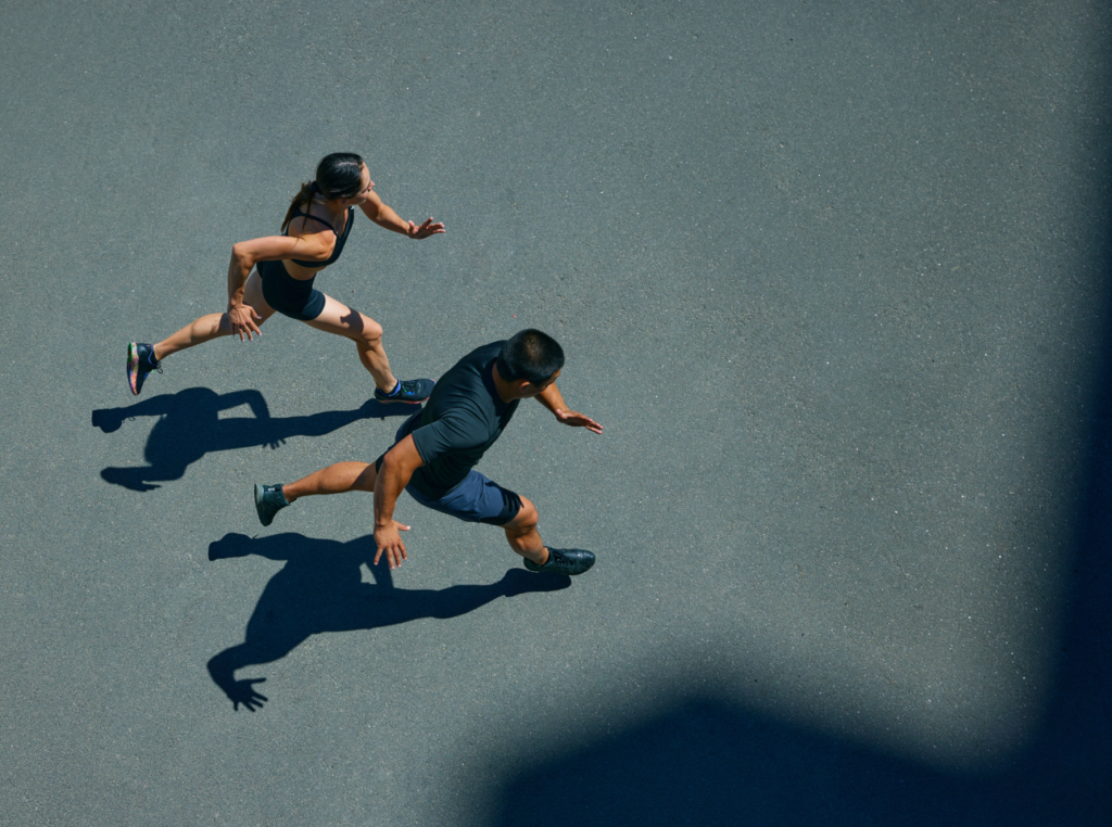 Overhead view of a man and woman running on a road, their strong shadows cast on the pavement, embodying the vigor and vitality that comes with enhanced cellular energy.