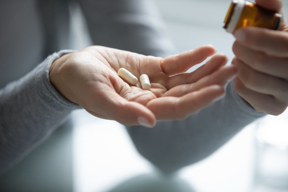 Close up of young female hands holding opened pill bottle and two soft-shelled capsules