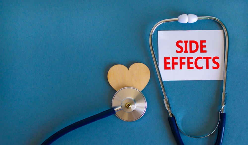 White card with words Side effects, beautiful blue background, wooden heart and stethoscope