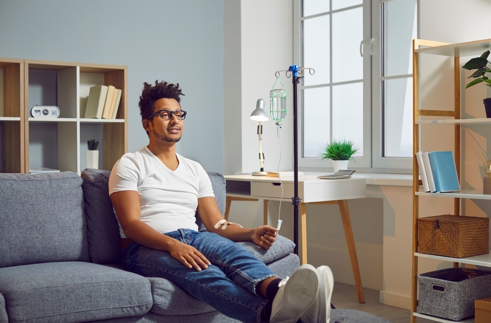 Young Afro American man with vitamin deficiency receiving modern intravenous anti stress nutrient and hydration therapy through sterile IV drip line infusion