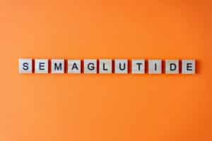 Word semaglutide. The phrase is laid out in wooden letters top view. Orange flat lay background