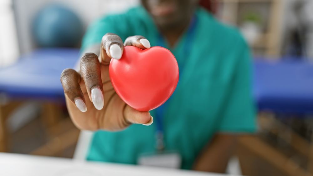 African american female healthcare professional holding a red heart in a clinic, symbolizing care and compassion in medicine.