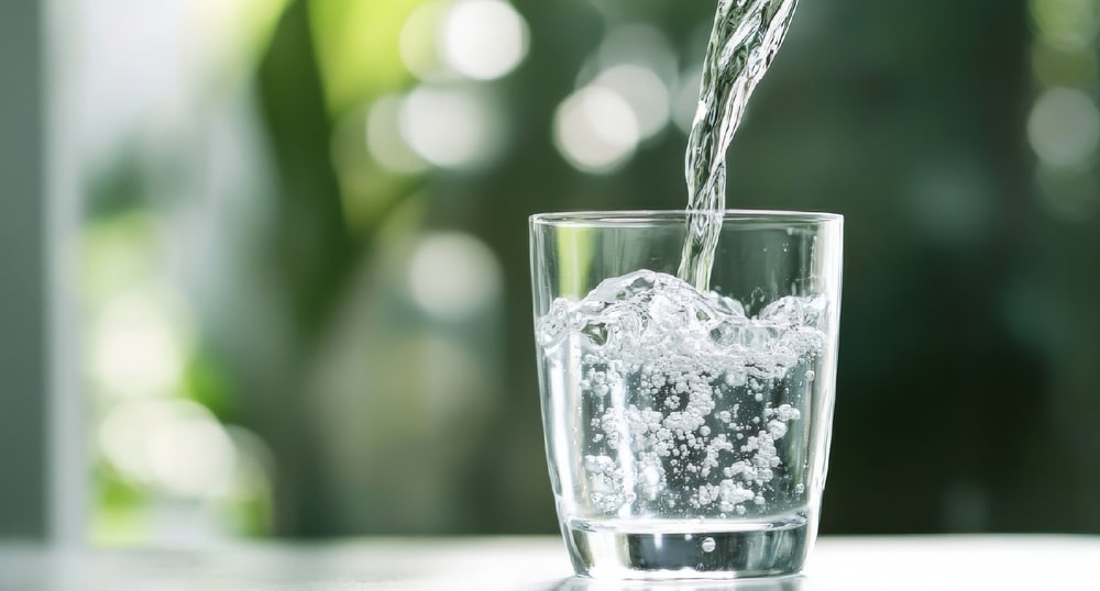 Pouring Water into a Glass Against a Green Blurred Background